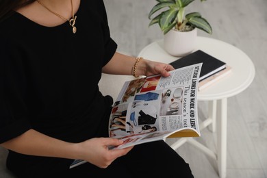 Photo of Young woman reading fashion magazine indoors, closeup