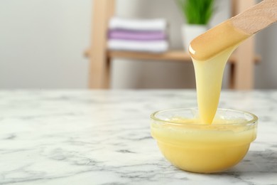 Photo of Spatula with wax on white marble table, closeup. Space for text