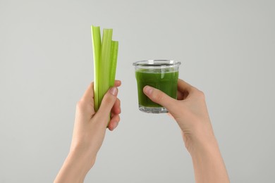 Photo of Woman holding glass of delicious celery juice and fresh vegetables on light grey background, closeup