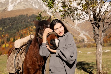 Young woman hugging horse in mountains on sunny day. Beautiful pet