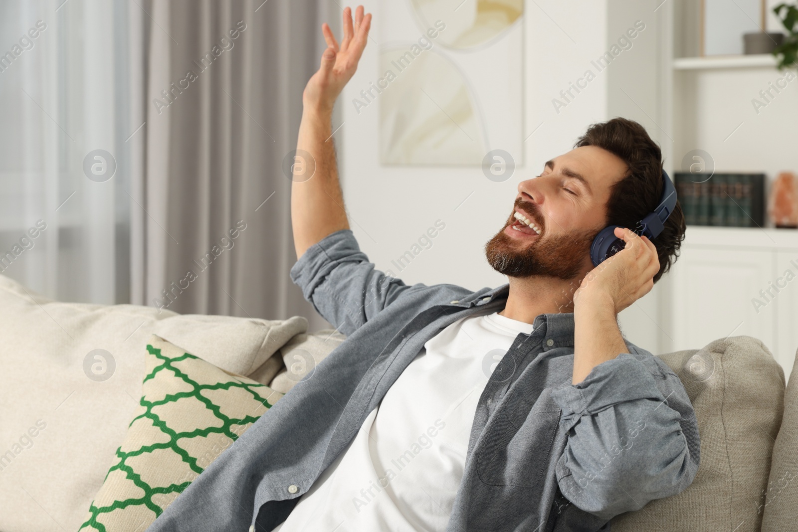 Photo of Happy man listening music with headphones on sofa indoors