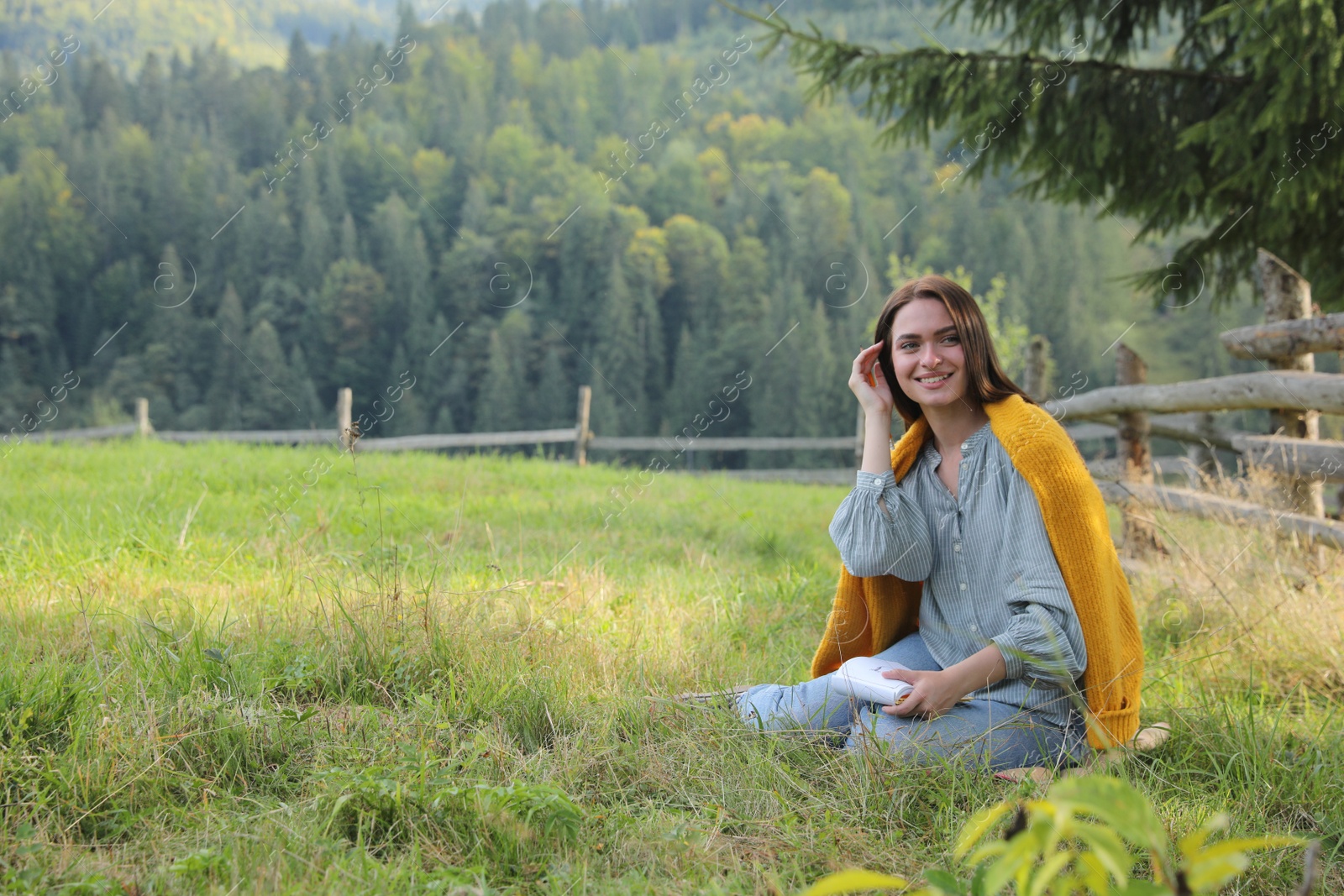 Photo of Beautiful young woman drawing with pencil in notepad on green grass