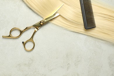Photo of Professional hairdresser scissors and comb with blonde hair strand on grey table, top view. Space for text