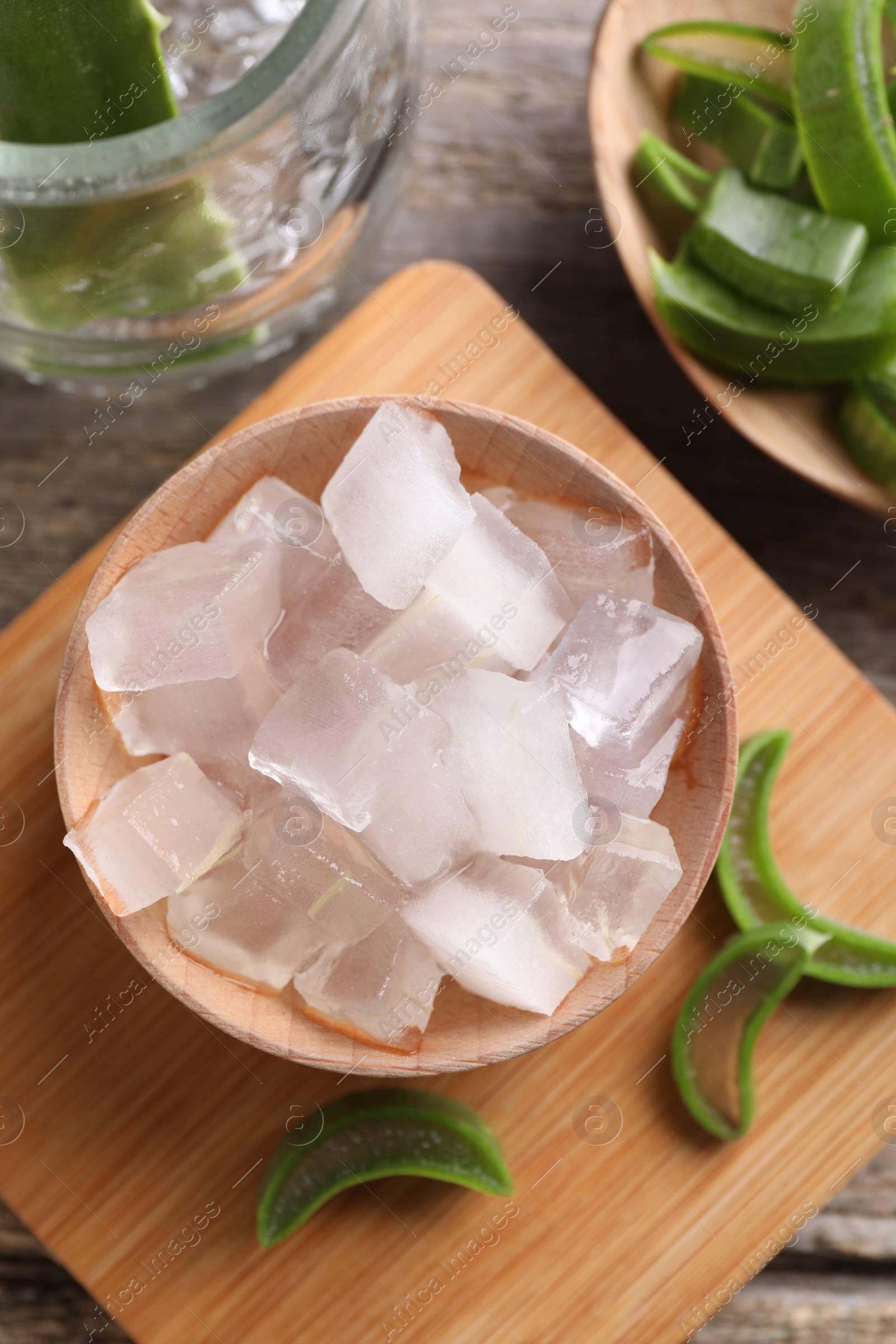 Photo of Aloe vera gel and slices of plant on wooden table, flat lay