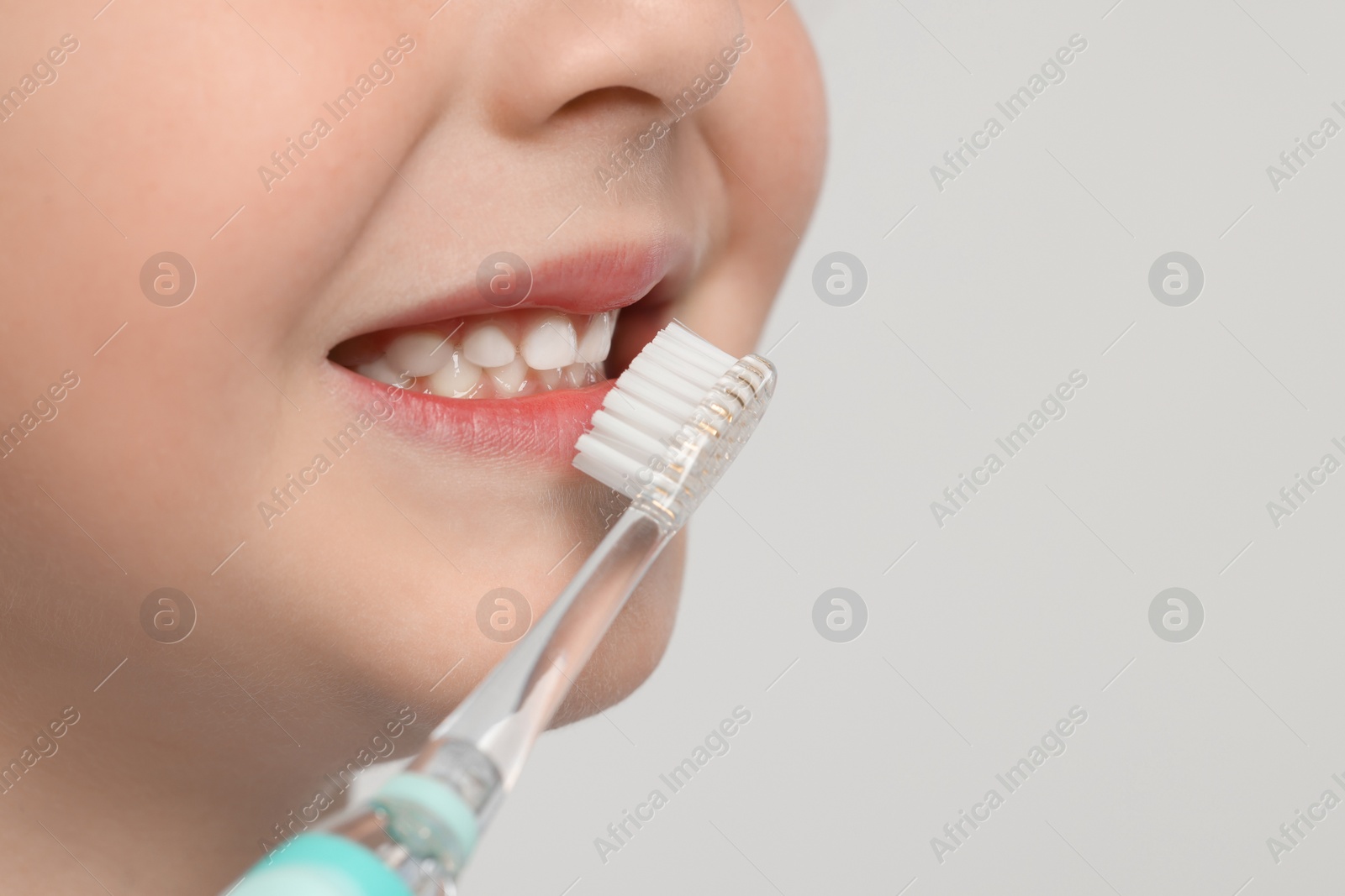 Photo of Cute little boy brushing his teeth with electric toothbrush on white background, closeup. Space for text