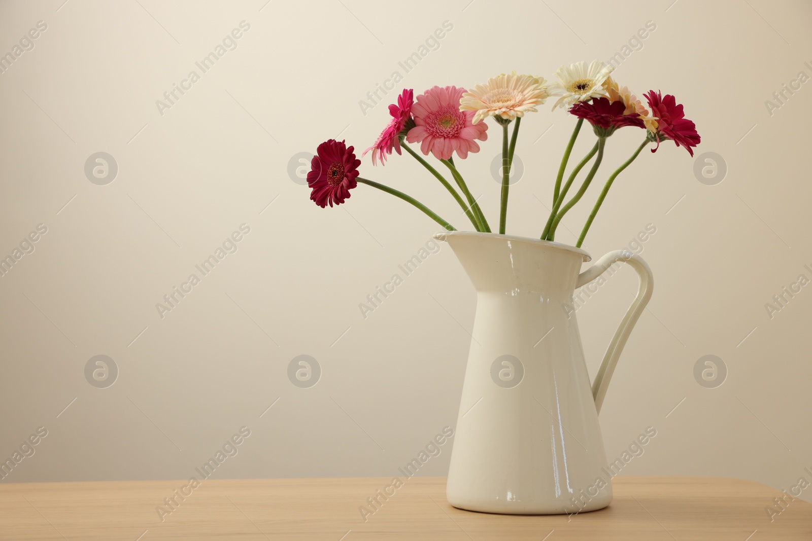 Photo of Jug with beautiful gerbera flowers on wooden table. Space for text