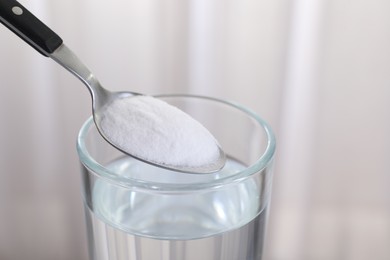 Adding baking soda into glass of water on light background, closeup