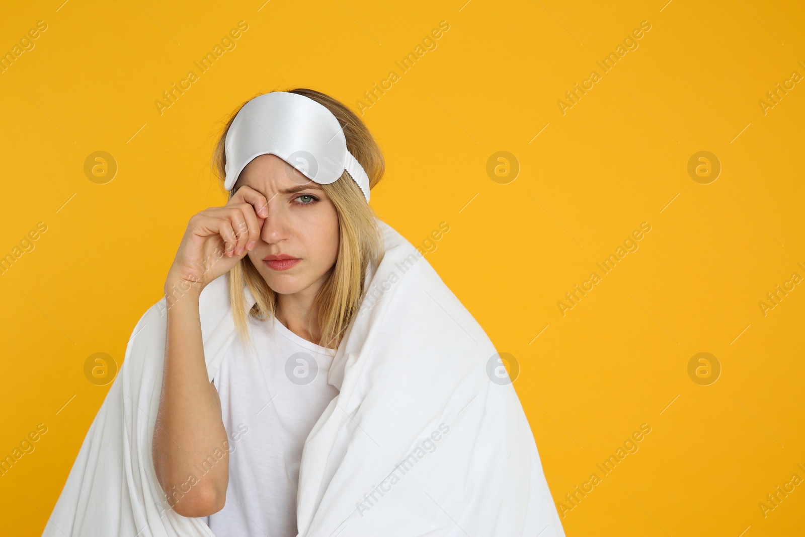 Photo of Young woman in sleeping mask wrapped with soft blanket on yellow background. Space for text