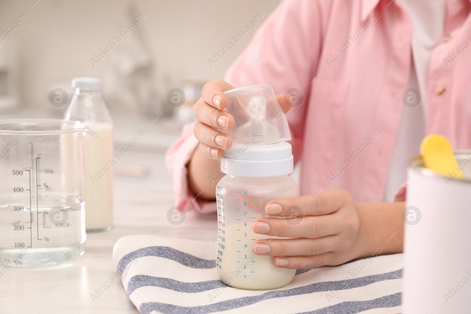 Photo of Woman with feeding bottle of infant formula at table indoors, closeup. Baby milk