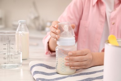 Woman with feeding bottle of infant formula at table indoors, closeup. Baby milk