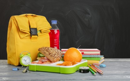 Image of Composition with lunch box and food on wooden table near blackboard