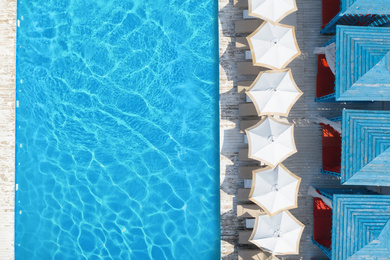 Image of Lounge chairs with umbrellas near swimming pool on sunny day, top view