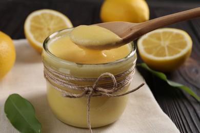 Photo of Taking delicious lemon curd from glass jar at wooden table, closeup