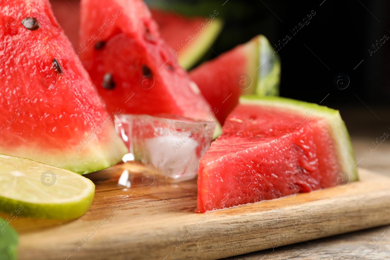 Photo of Board with juicy watermelon, ice and lime slices on wooden table, closeup