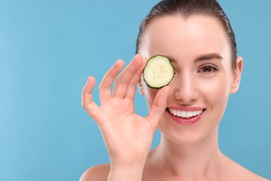 Photo of Beautiful woman covering eye with piece of cucumber on light blue background. Space for text