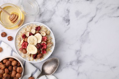 Photo of Delicious oatmeal with freeze dried berries, banana and hazelnuts served on white marble table, flat lay. Space for text