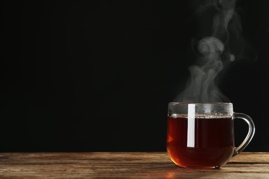 Photo of Cup with steam on wooden table against black background. Space for text