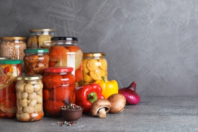 Photo of Jars of tasty pickled vegetables on grey table. Space for text