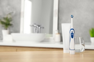 Photo of Electric toothbrush, tube with paste and glass of water on wooden table in bathroom. Space for text