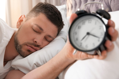 Man with alarm clock sleeping at home in morning