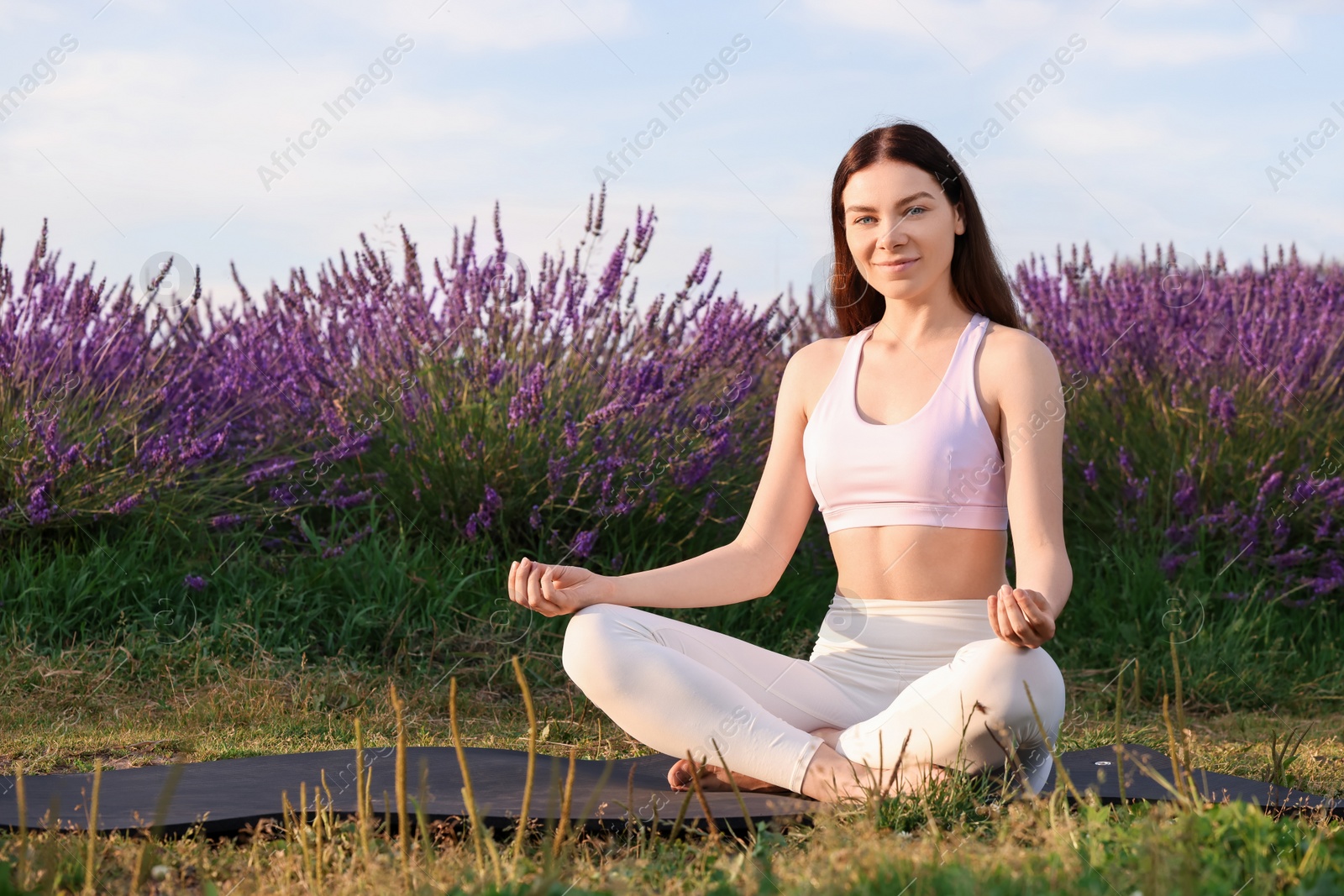 Photo of Beautiful woman practicing yoga near blooming lavender outdoors. Space for text