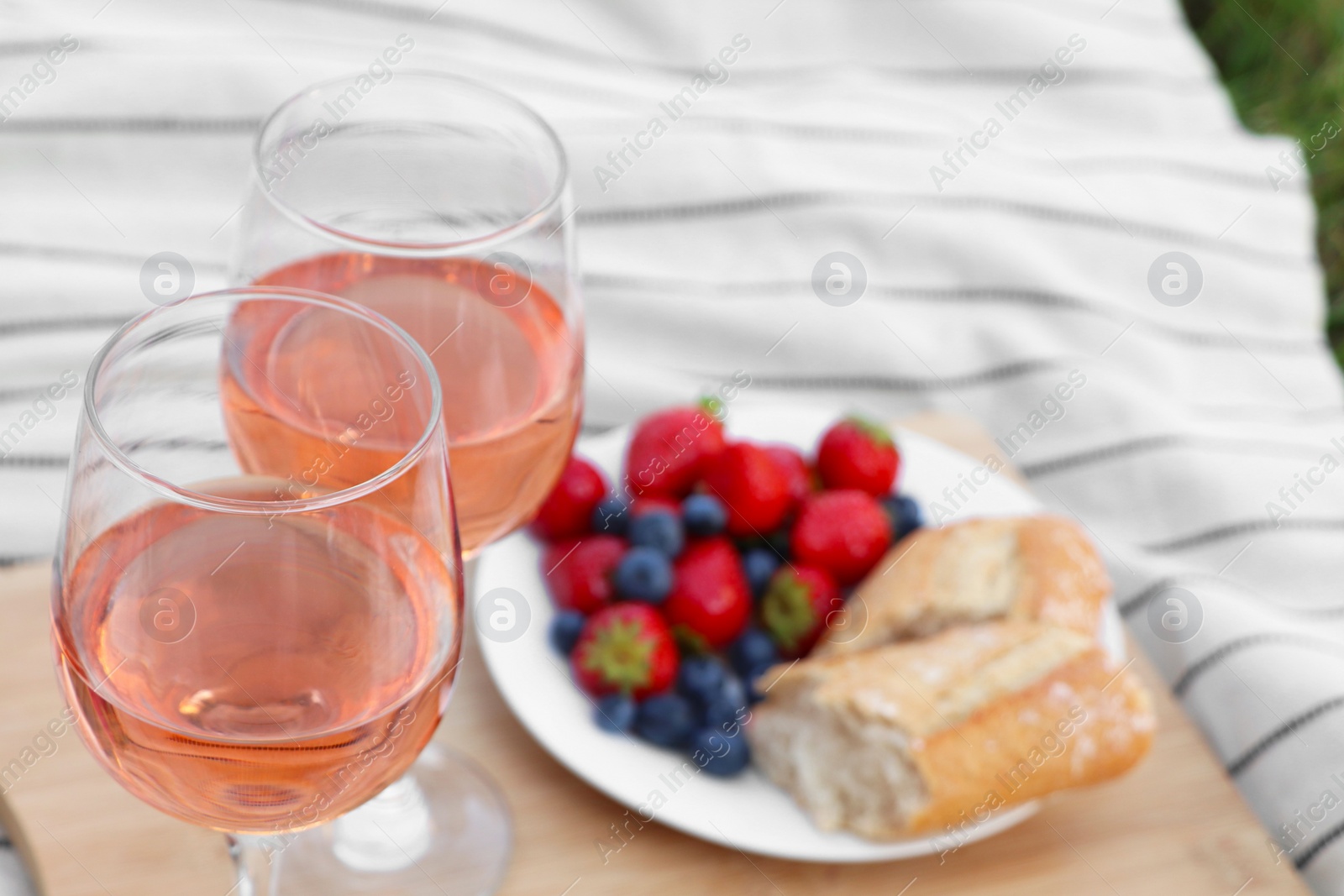 Photo of Glasses of delicious rose wine and food on white picnic blanket, closeup