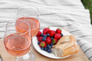 Glasses of delicious rose wine and food on white picnic blanket, closeup