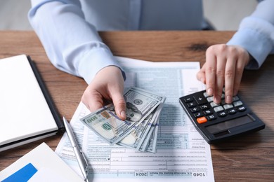 Photo of Payroll. Woman with dollar banknotes and calculator planning budget at wooden table, closeup