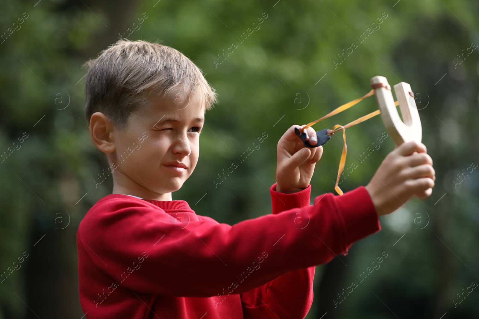 Photo of Little boy playing with slingshot in park