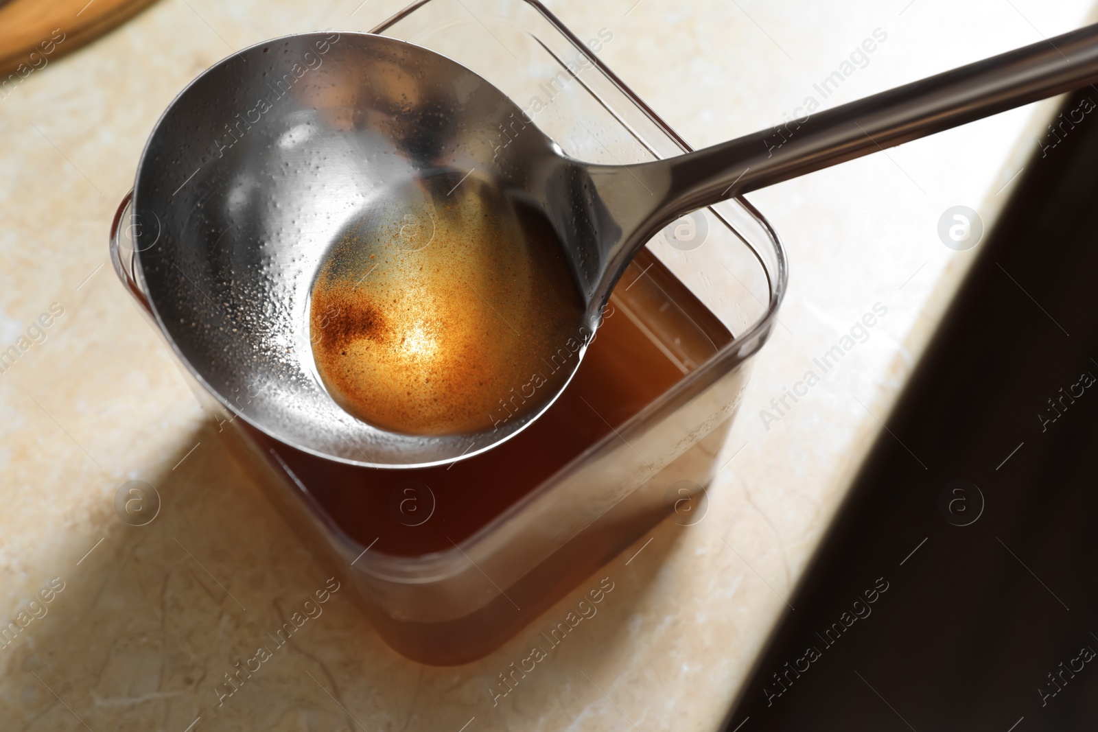 Photo of Container and ladle with used cooking oil on beige table