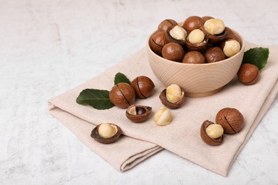 Photo of Bowl with organic Macadamia nuts and green leaves on white textured table