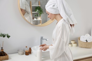 Photo of Beautiful young woman using body cream in bathroom, space for text