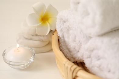 Photo of Spa composition. Rolled towels, massage stones, burning candle and plumeria flower on table, closeup