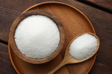 Photo of Granulated sugar in bowl and spoon on wooden table, top view