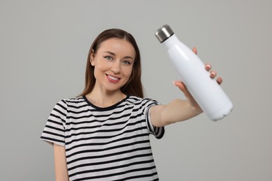 Beautiful young woman with thermos bottle on light grey background