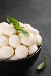 Tasty mozzarella balls and basil leaves in bowl on black table, closeup