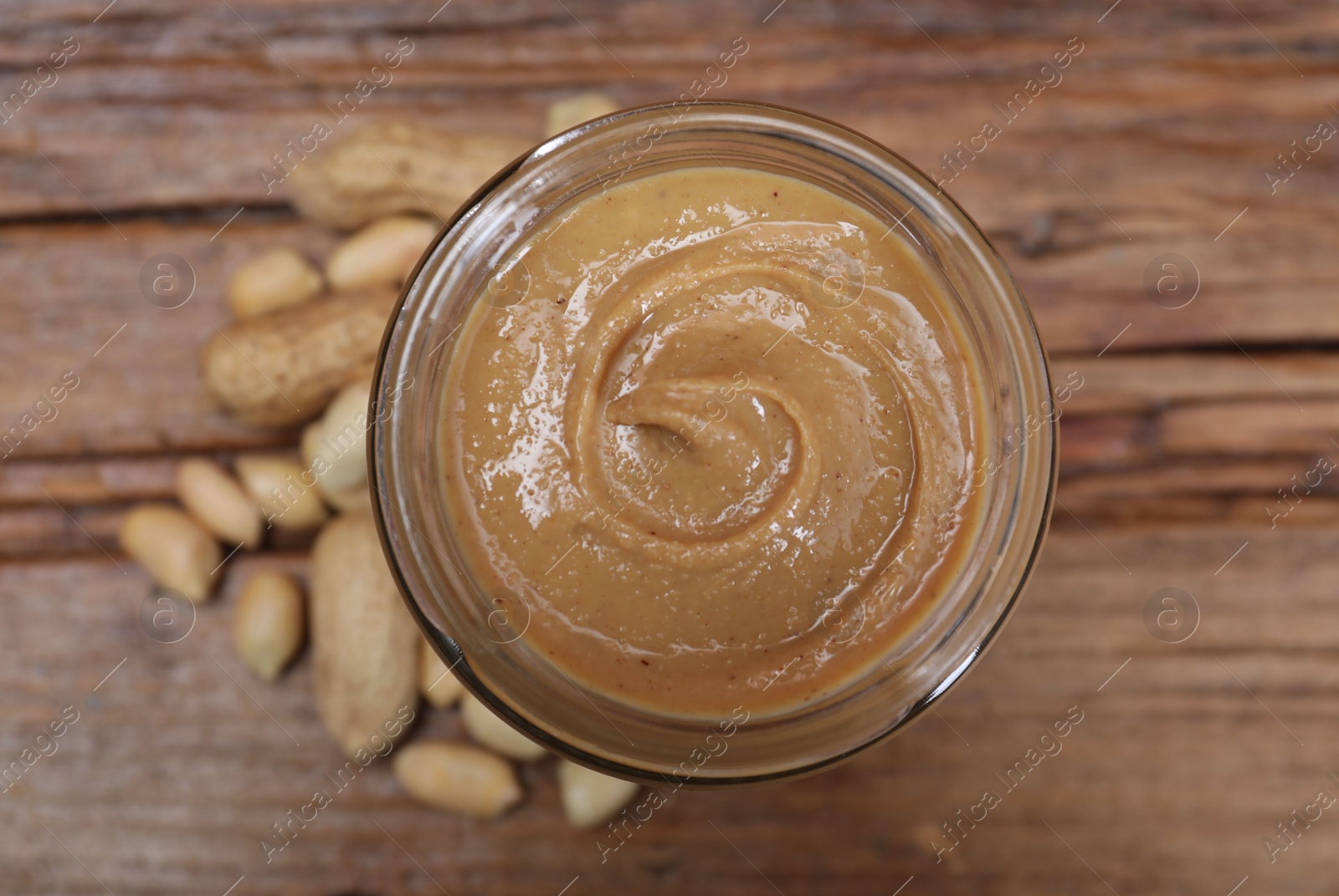 Photo of Tasty peanut nut paste in jar on table, top view