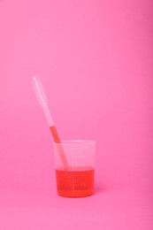 Photo of Beaker with liquid and stirring rod on bright pink background. Chemical experiment toy for kids