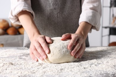 Woman kneading dough at table in kitchen, closeup