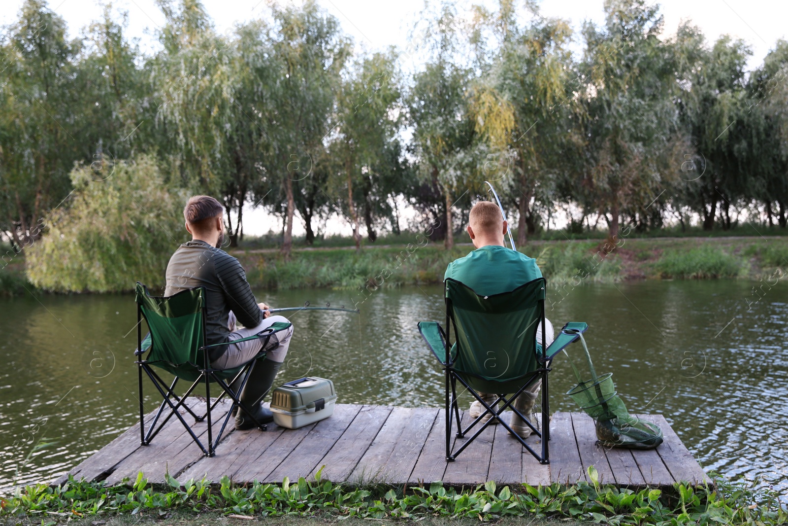 Photo of Friends fishing on wooden pier at riverside. Recreational activity