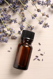 Bottle of essential oil and lavender flowers on white wooden table, flat lay