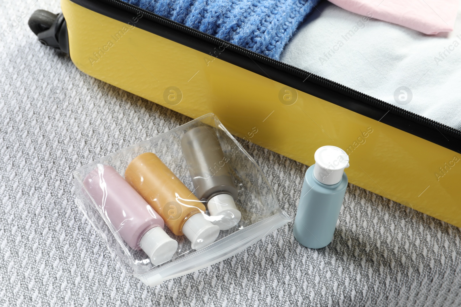 Photo of Plastic bag of cosmetic travel kit and suitcase on bed