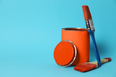 Photo of Can of orange paint and brushes on turquoise background. Space for text