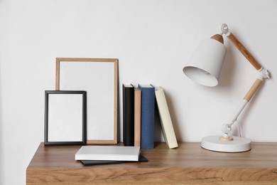 Stylish modern desk lamp, books and frames on wooden table near white wall indoors