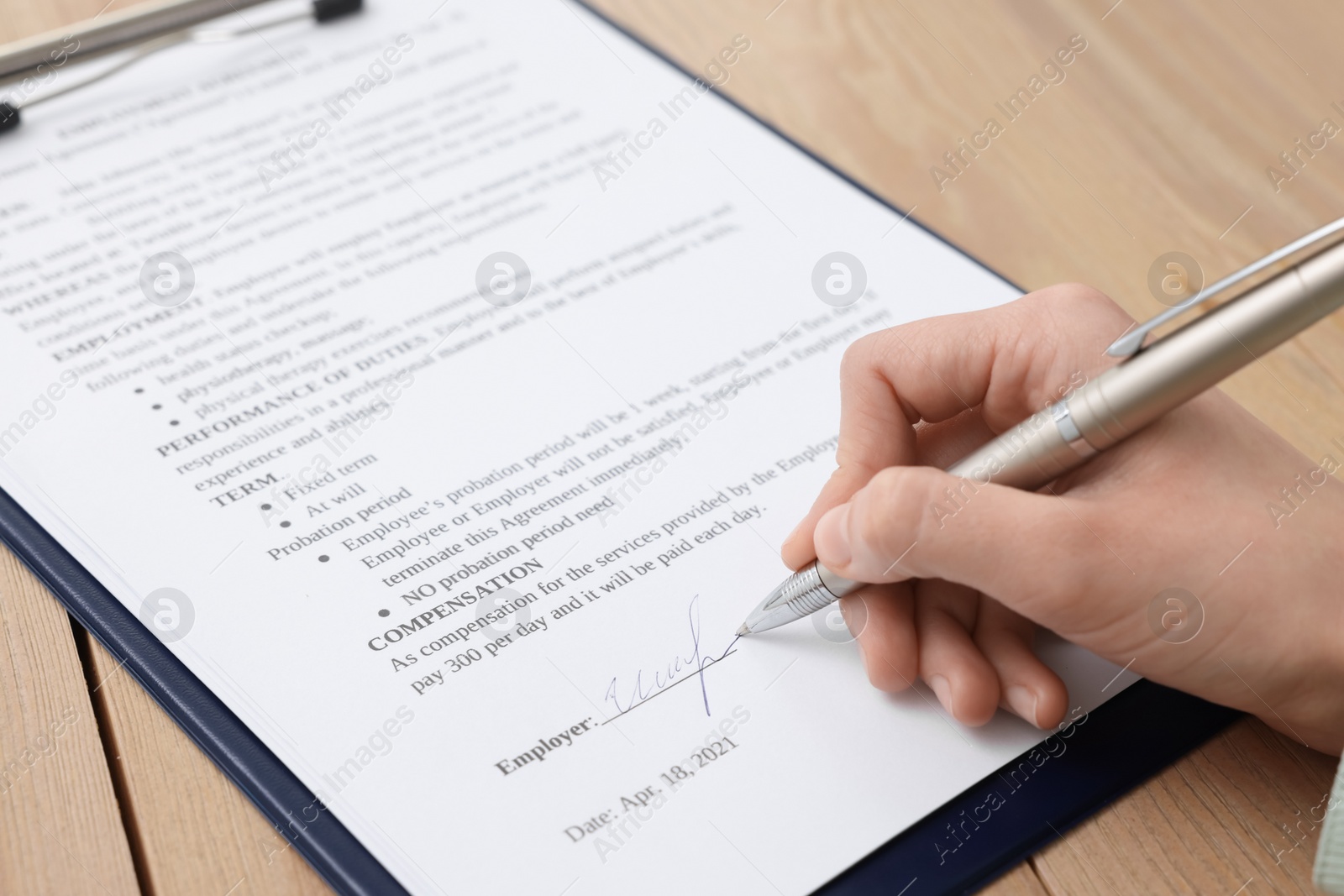 Photo of Woman signing contract at wooden table, closeup.