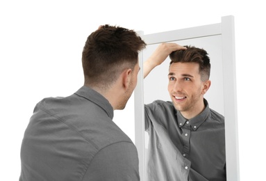 Young man looking at himself in mirror on white background
