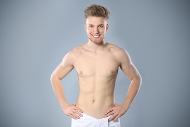 Portrait of young man with slim body in towel on grey background. Space for text