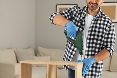 Man with electric screwdriver assembling wooden furniture at home, closeup. Space for text