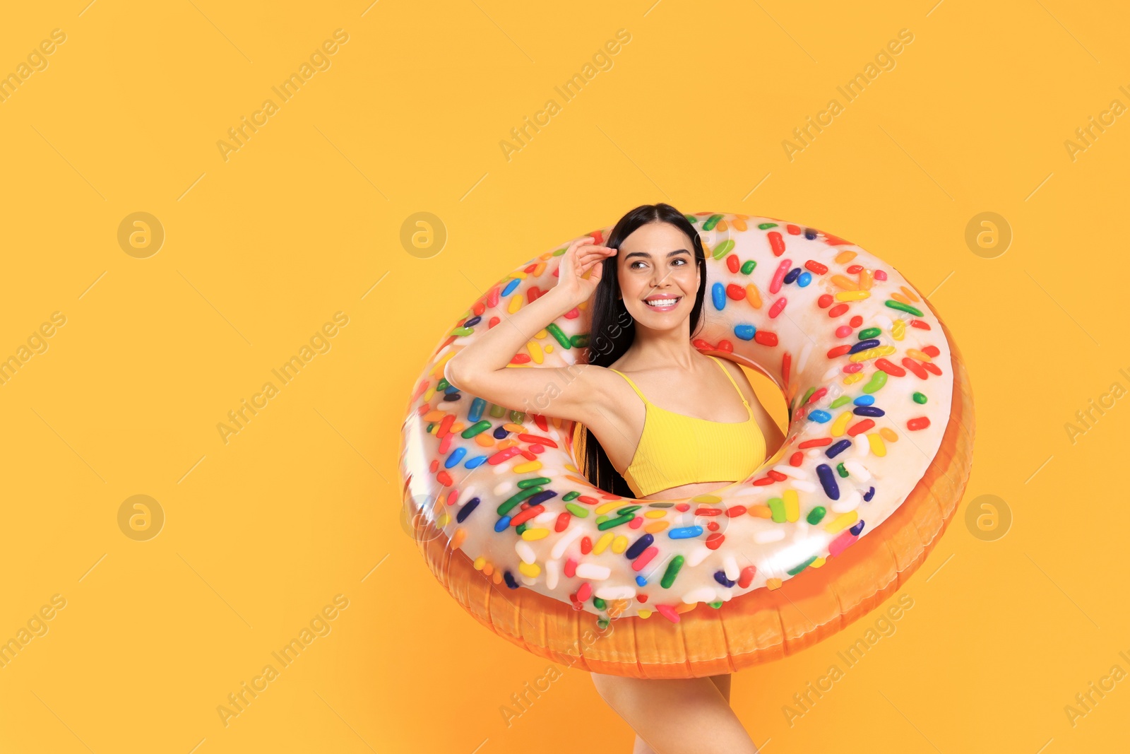 Photo of Happy young woman with beautiful suntan and inflatable ring against orange background