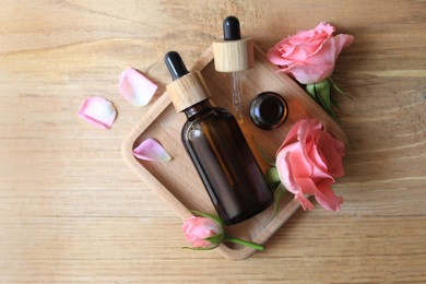 Photo of Flat lay composition with essential rose oil and flowers on wooden table